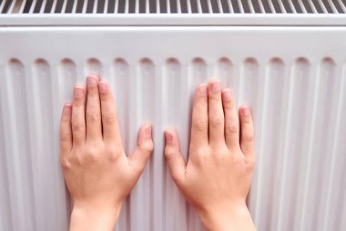 Kız ellerini radyatörde ısıtıyor.