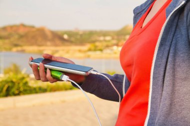 Bir kız dış güç bankasından şarj olurken açık havada akıllı telefon kullanıyor..