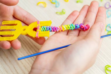 Lastik bantlı dokuma. Dokuma tezgahıyla lastik bantlar örüyorlar. Lastik bileklik takan bir kızın elleri.