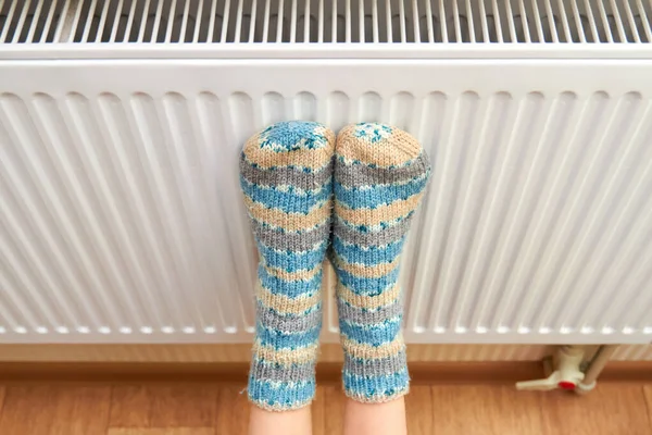 Mavi yün çoraplı bir kız ayaklarını radyatörde ısıtıyor.