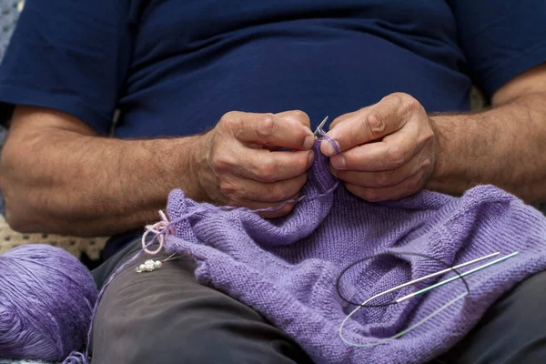 Closeup of elderly man knitting a purple sweater. Knitting like hobbies handmade.