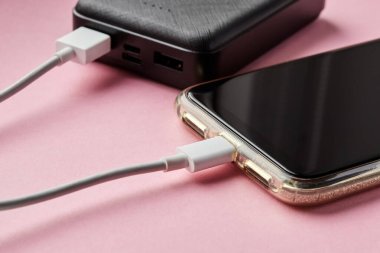 Güç bankası akıllı telefonu pembe bir yüzeyde USB kablosu kullanarak şarj ediyor. Yakın çekim, seçici odaklanma