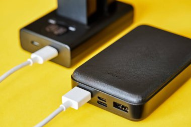 Elektrik bankası bataryalarını sarı arka planda USB kablosu kullanarak şarj ediyor. Yakın çekim, seçici odaklanma