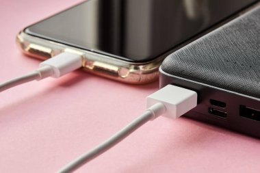 Güç bankası akıllı telefonu pembe bir yüzeyde USB kablosu kullanarak şarj ediyor. Yakın çekim, seçici odaklanma