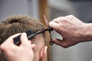 Profesyonel berber, berber dükkanında makas ve tarak kullanarak genç adamın saçını kesiyor. Yakın çekim, seçici odaklanma