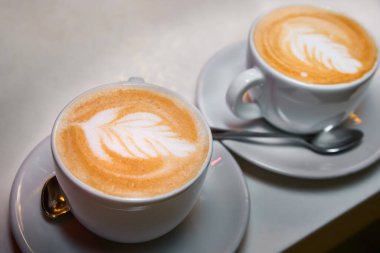 İki fincan kahve. Beyaz bardaklarda bir desenli latte.
