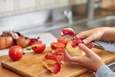 Kız kırmızı bir elmadan bir bıçakla kabuk keser. Mutfakta yemek hazırlarken yiyecek atıkları ve ekstralar. Yakın çekim, seçici odaklanma
