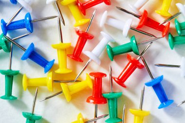 Renkli kırtasiye düğmeleri açık arkaplanda serili. Eğitim için karanfiller. Kağıt iliştiriyorum. Ofis kırtasiyesi. Kağıt eklemek için keskin iğne.