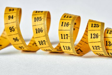 Beyaz zemin üzerinde uzunluk ve genişlik ölçümü için siyah şekilli sarı renkli santimetre. Tasarımınız için terzinin şeridini ölçüyorum. Yakın çekim, seçici odaklanma