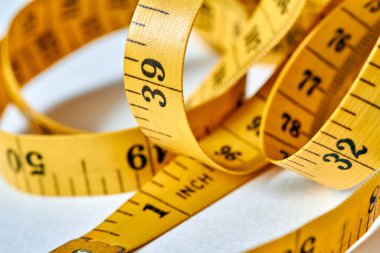 Beyaz zemin üzerinde uzunluk ve genişlik ölçümü için siyah şekilli sarı renkli santimetre. Tasarımınız için terzinin şeridini ölçüyorum. Yakın çekim, seçici odaklanma