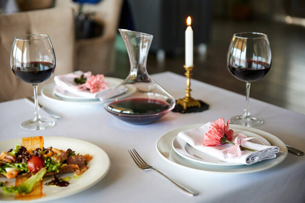 A served restaurant table with glasses of red wine and appetizer awaits guests. Close-up, selective focus