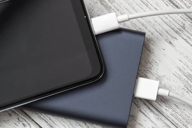 Akıllı telefon, dış güç bankasından kablo ile gri ahşap arka planda şarj oluyor. Yakın çekim, seçici odaklanma