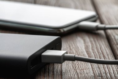 Akıllı telefon dış elektrik bankasından kabloyla kahverengi ahşap arka planda şarj oluyor. Yakın çekim, seçici odaklanma
