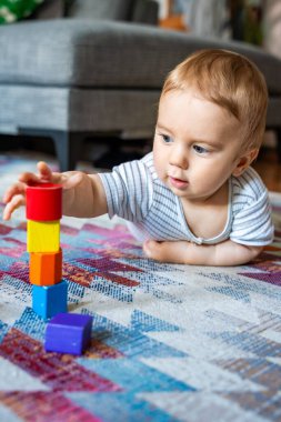 Çizgili kıyafetli bir bebek desenli halıda renkli ahşap bloklarla oynuyor, rahat bir arka plan, erken öğrenim ve gelişme kavramı