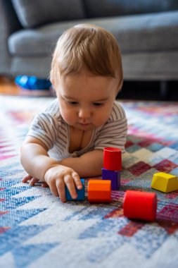 Çizgili kıyafetli bir bebek desenli halıda renkli ahşap bloklarla oynuyor, rahat bir arka plan, erken öğrenim ve gelişme kavramı