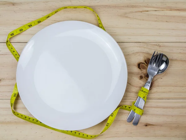 Empty plate with measure tape, spoon and fork. Diet food on wood — Stock Photo, Image