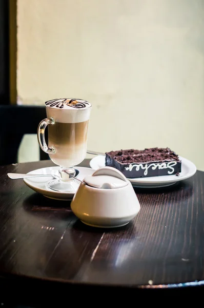Taza de capuchino, un pedazo de pastel de chocolate en el plato de mesa oscura — Foto de Stock