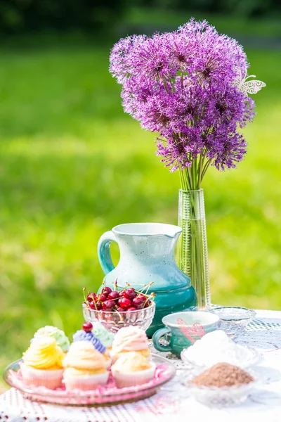 Délicieux cupcakes, cerise et cruche sur la table dans le jardin — Photo