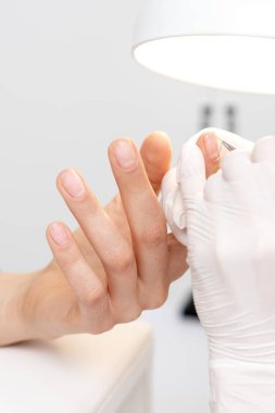 Profesyonel manikür ustası genç bir kadının tırnağına pembe jel kalemle süslemeler çiziyor.