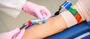 Pembe eldivenli hemşire laboratuardaki kadın hastadan kan örneği alıyor.