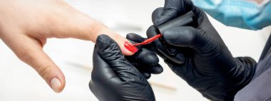 Profesyonel manikür ustası kadın tırnaklarını ojeyle boyuyor.