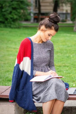 Öğrenci genç bayan parktaki bankta günlük tutuyor.