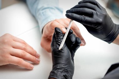 Manikür ustası tarafından manikür yaptıran genç bir kadının, manikür salonundaki tırnak törpüsüyle yakın çekimi.