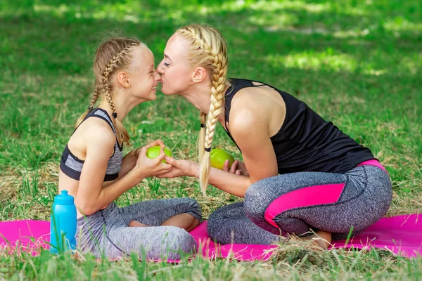 妈妈吻着女儿的鼻子 把绿色的苹果放在公园的草地上 — 图库照片