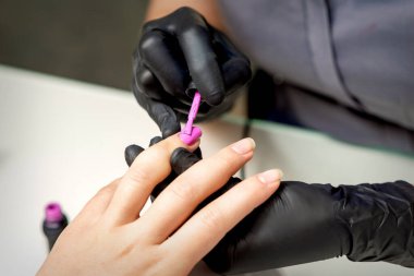 Manikür ustası, kuafördeki kadın tırnaklarına pembe oje sürüyor.