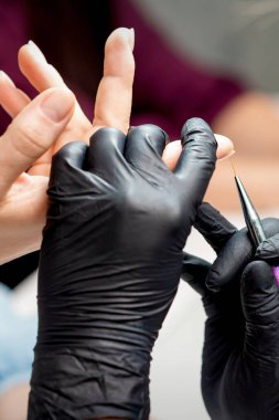 Manikür ustası, manikür salonundaki kadın tırnağının kenarına mor jel kalemle süslemeler yapıyor.