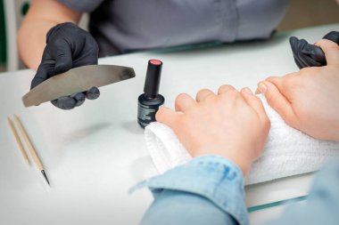 Kadın eli, manikürcüdeki manikürcünün elinde törpü ile işleme hazırlanıyor.