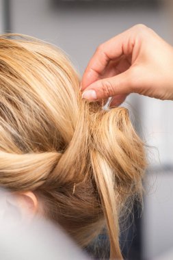 Kadın kuaförün elinin yakından görünüşü, kuaförde genç sarışın bir kadının saçını yapıyor.