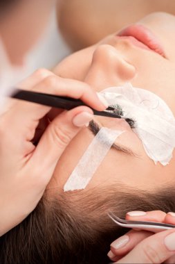 Beyaz kadın güzellik salonunda kirpik uzatma prosedürü uyguluyor.