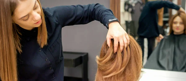 Back view of hairdresser checks red or brown hairstyle of young woman in hair salon. Soft focus