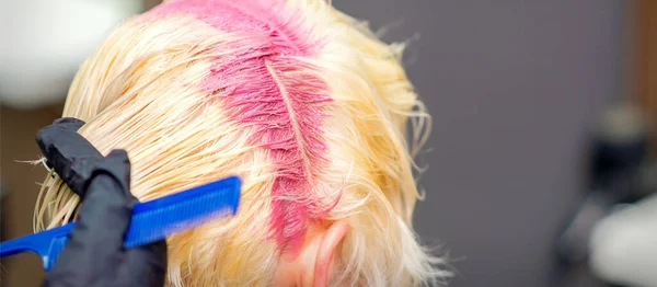 ヘアサロンで若いブロンドの女性の髪の根にピンク色の髪の色 選択的焦点 — ストック写真