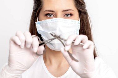 Beyaz arka planda manikür aletleri tutan beyaz koruyucu maskeli manikür ustasının portresi