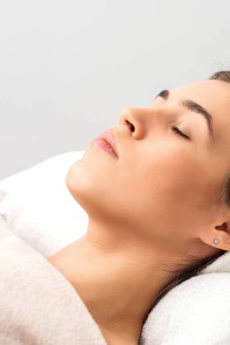 Güzellik salonunda estetik ameliyat beklerken kapalı gözlerle güzellik masasında uzanan genç bir kadının yan görüntüsü.