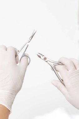Manikür aletleri beyaz arka planda beyaz koruyucu eldivenler giyen manikür ustasının ellerinde.