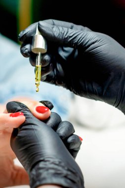 Manikür ustası, manikürcüdeki kadın tırnaklarına pipetle yağ sürüyor.