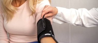 Hemşire ya da kadın doktor hastanede genç bir kadının koluna tonometre takıyor.