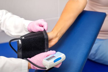 Hemşire ya da kadın doktor hastanede genç bir kadının koluna tonometre takıyor.