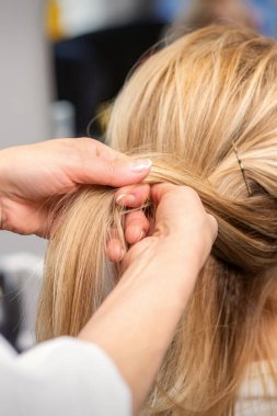 Güzellik salonunda müşterinin saçını ören kuaförün ellerini kapat.