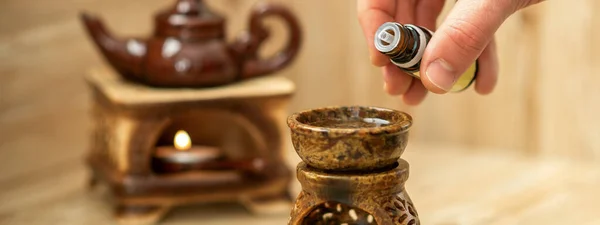 Hand of therapist pours drops of essential oil to a ceramic diffuser in spa salon