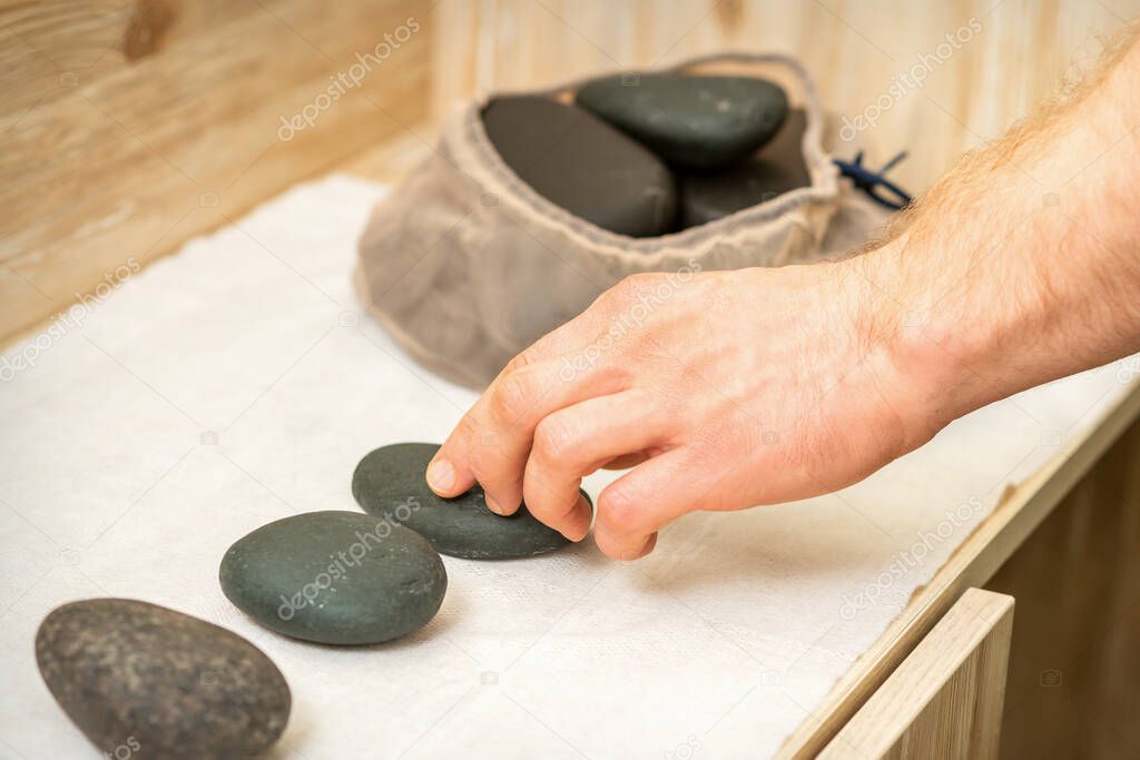 Hand of masseur takes hot black massage stones from table in spa