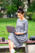 Gyönyörű fiatal nő ül egy padon egy laptop és dolgozik, vagy tanul a szabadban