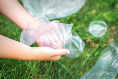 Çocuğun elleri çimlerdeki kullanılmış plastik çatal bıçaklardan parkı temizliyor.