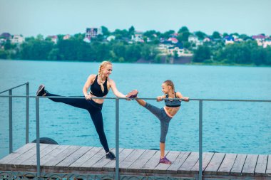 Kadın ve çocuk spor egzersizleri yapıyorlar. Rıhtımda bacaklarını açıyorlar. Gölde.