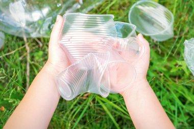 Çocuğun elleri çimlerdeki kullanılmış plastik çatal bıçaklardan parkı temizliyor.