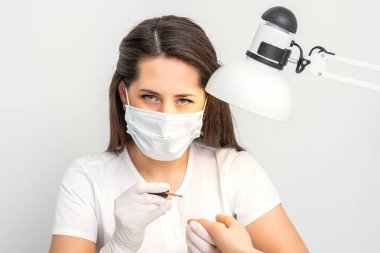 Beyaz koruyucu maskeli manikür ustasının portresi güzellik salonunda çalışıyor.