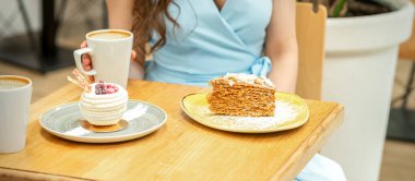 Bir kadının arka planındaki tabakta, bir kafede bir fincan kahveyle tatlı farklı kek parçaları.